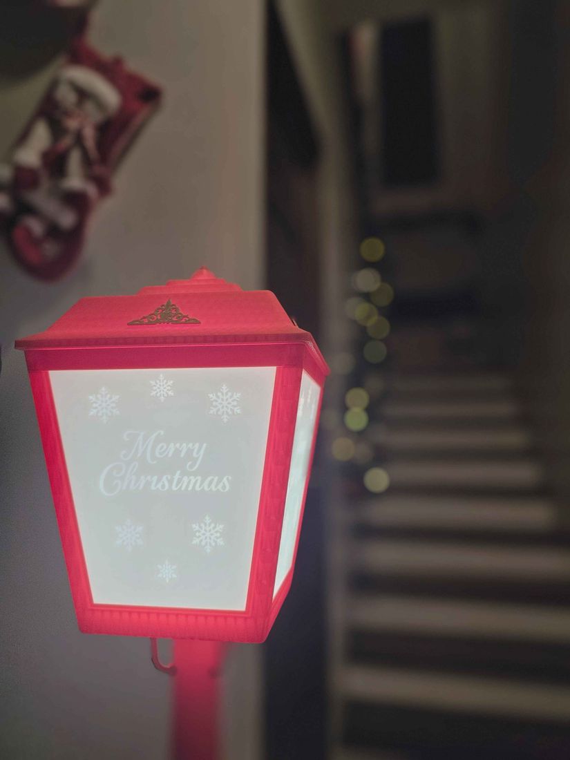 A red 3D printed lantern lit from inside, with snowflakes and a custom greeting showing through the panel wall.