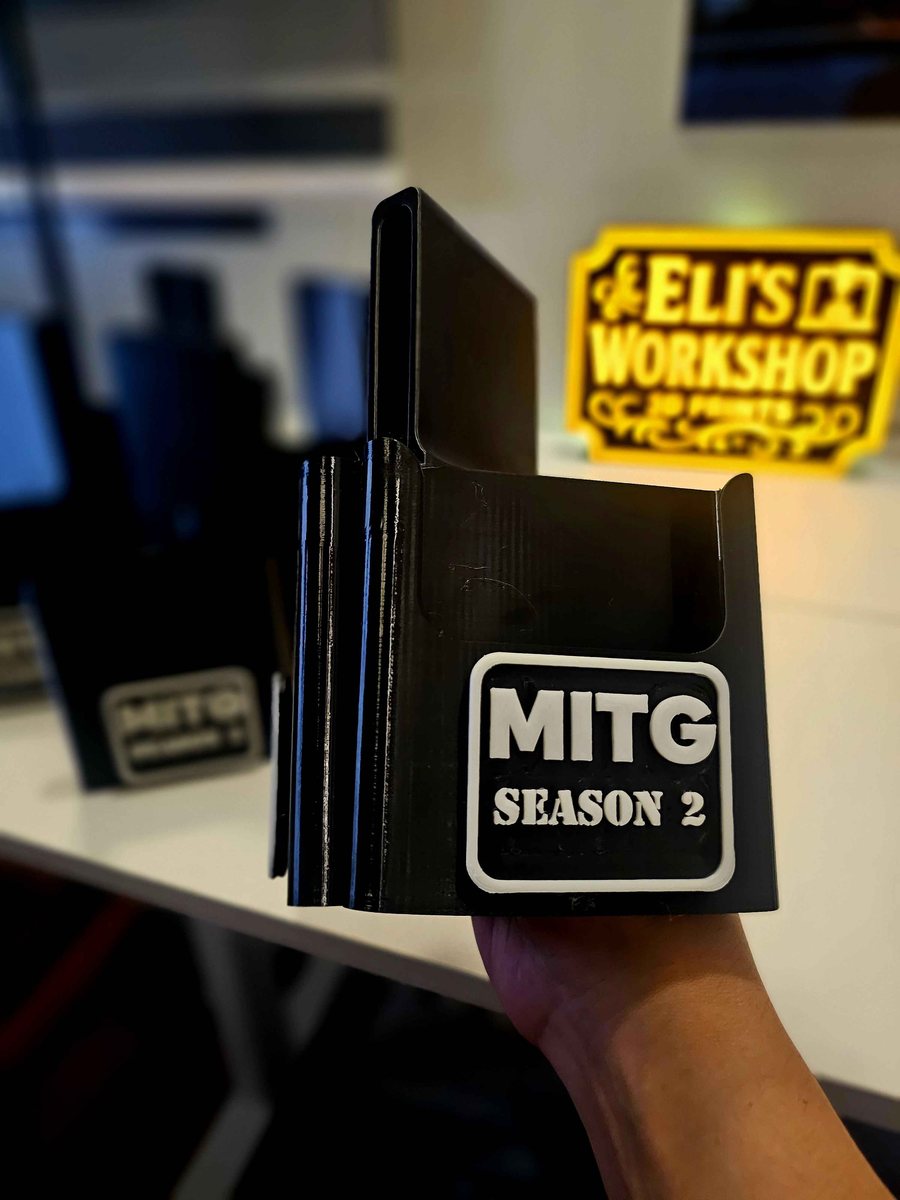 Close-up of a black 3D printed card holder held in a hand, showing a white logo badge printed in raised relief rather than painted on.